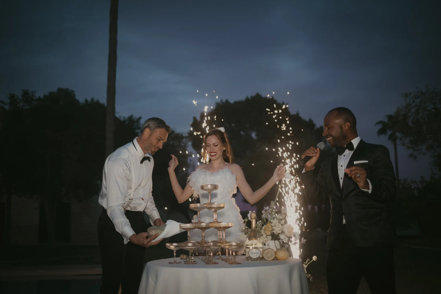 Hochzeitsparty: Brautpaar und Hochzeitssänger tanzen. Der Bräutigam schenkt den Champagner ein.