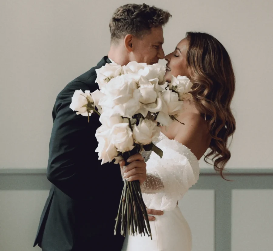 glückliches Hochzeitspaar küsst sich und versteckt sich hinter dem Brautstrauß
